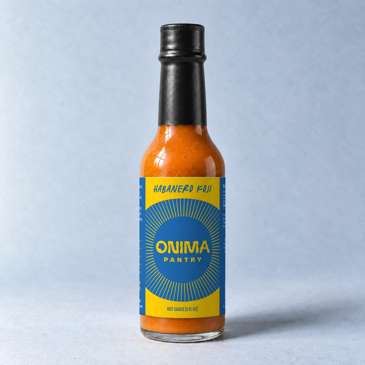 ONIMA Habanero Koji bottle with its yellow and blue label on a pale blue surface.
