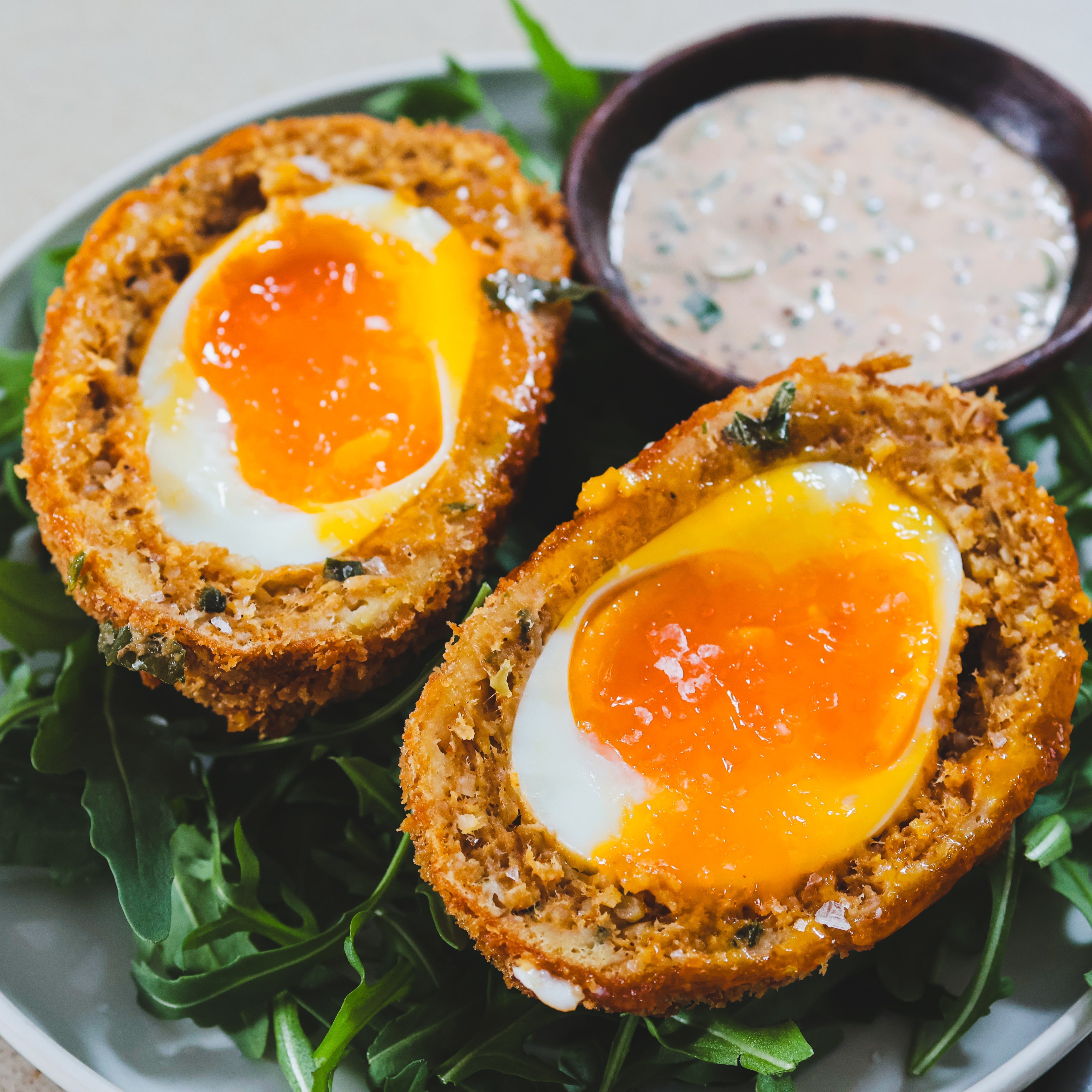 Crispy Cajun Scotch Egg sliced in half, revealing a soft-boiled yolk wrapped in boudin sausage, coated in golden panko breadcrumbs, and served with a creamy Cajun Sumac sauce.