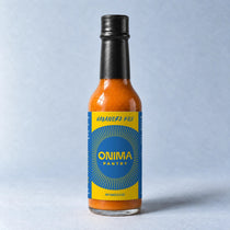 ONIMA Habanero Koji bottle with its yellow and blue label on a pale blue surface.