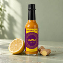 ONIMA Lemon Ginger Jerk hot sauce bottle with its purple and yellow label, beside lemon and ginger.