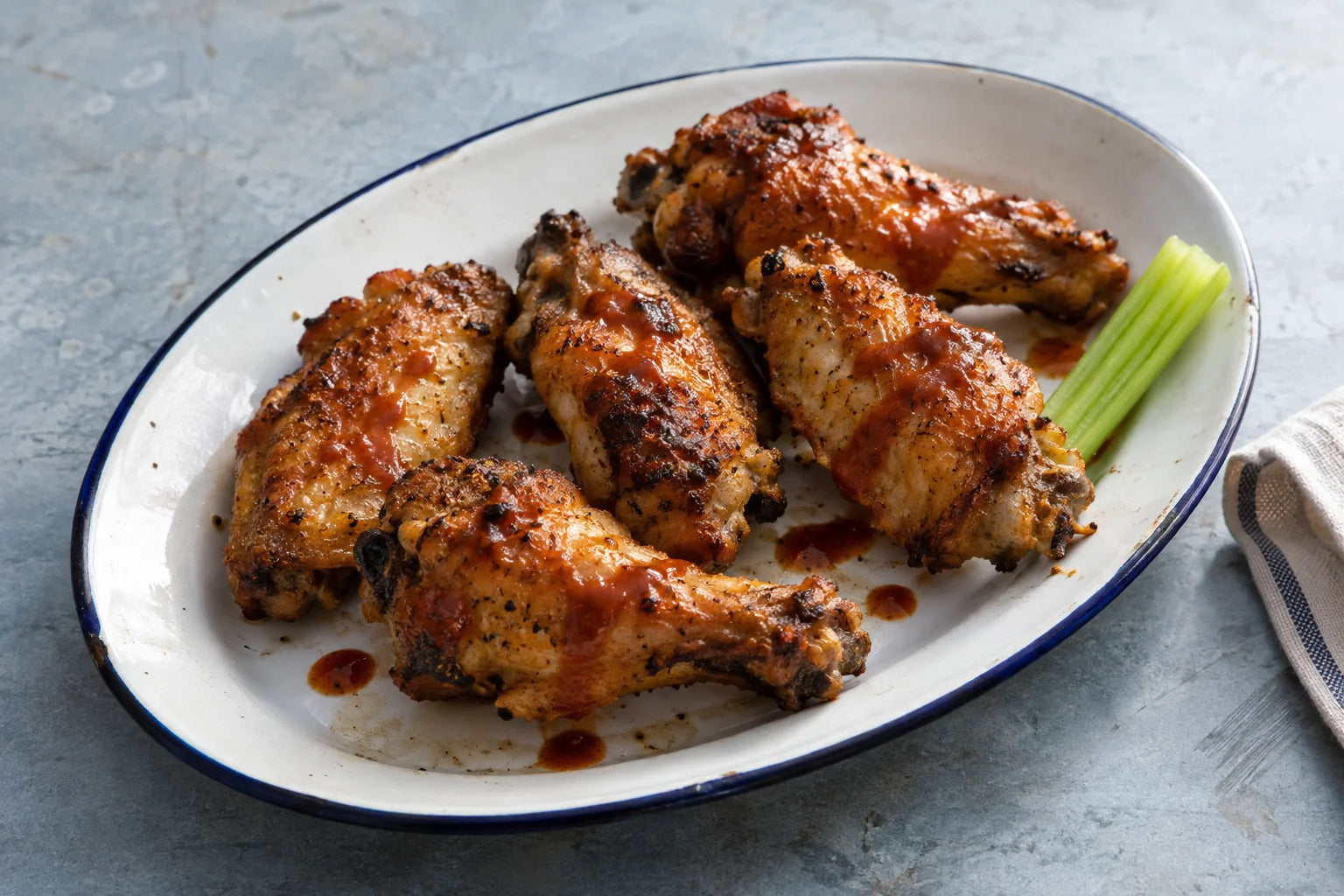 Crisp chicken wings with Cajun Sumac hot sauce on an oval enamel platter.