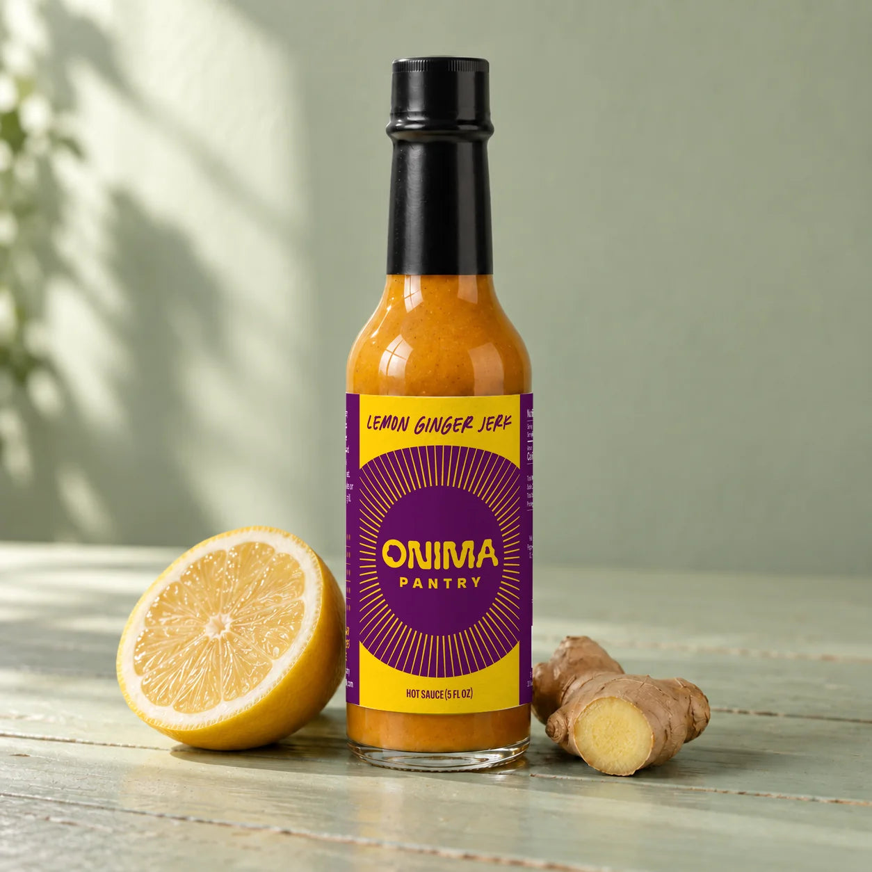 ONIMA Lemon Ginger Jerk hot sauce bottle with its purple and yellow label, beside lemon and ginger.