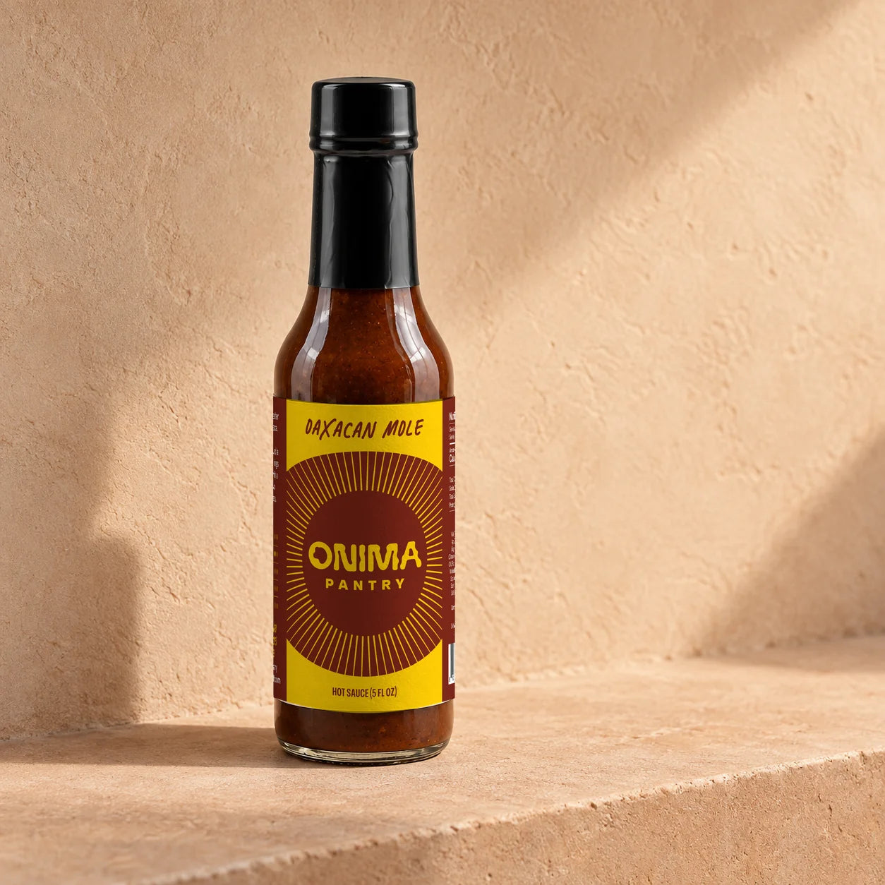 ONIMA Oaxacan Mole hot sauce bottle with its brown and yellow label on a plaster ledge.